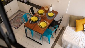 A compact dining area with a wooden table set for four, surrounded by turquoise chairs. A kitchen with a black countertop and a sink is visible in the background. - Hotel comfort in a prestigious residence (Chéraga)