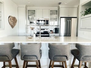 Una cocina moderna con armarios blancos, electrodomésticos de acero inoxidable y una isla central con taburetes de bar.