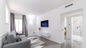 A modern living room with a grey sofa, a flat-screen TV, a white console table, and a marble bathroom door. - iRoome Rome (Roma)