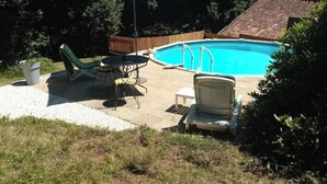 En baghave med swimmingpool, overdækket terrasse og udendørs møbler.