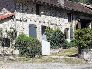 A stone building with multiple windows and doors, surrounded by greenery and a gravel path. - "Etangs des Cygnes" Vacation Home (Bussière-Galant)