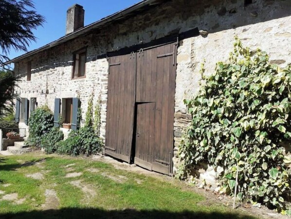 A stone building with a large wooden door, a small window, and a staircase leading to the entrance. - "Etangs des Cygnes" Vacation Home (Bussière-Galant)
