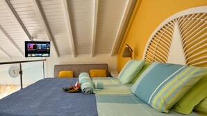 A bedroom with a bed, a TV mounted on the wall, and a window with a view of the outside. - Detached yellow studio in front of the pool 150m from the beach! (saint martin)