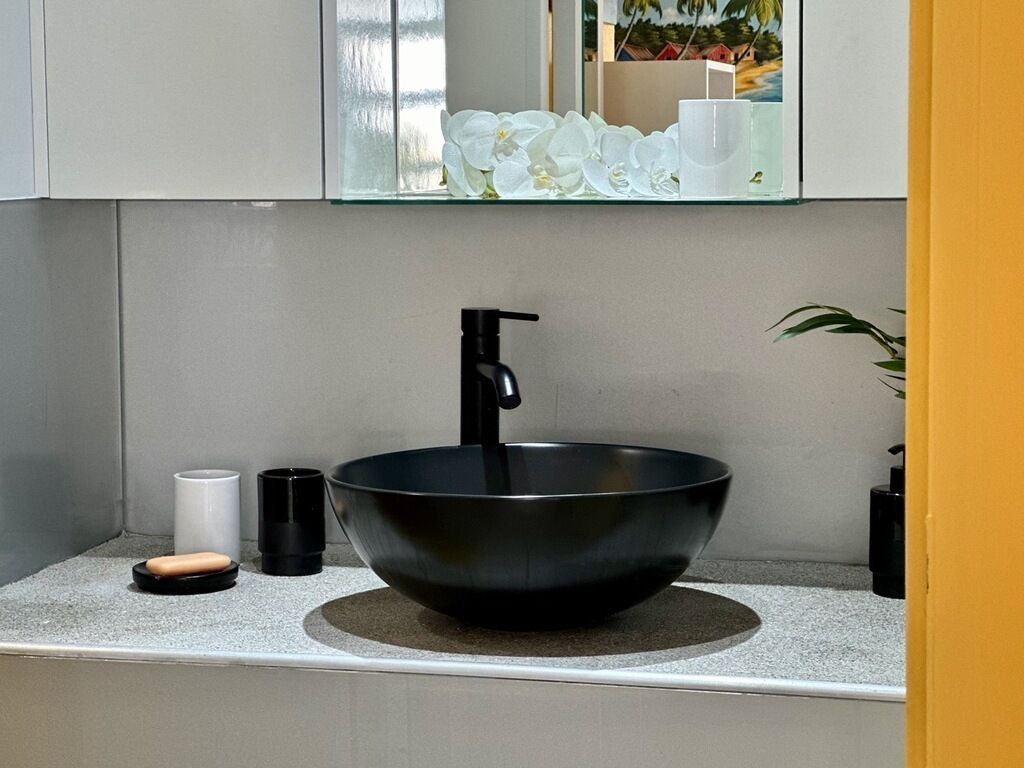 Ein modernes Badezimmer mit einem schwarzen Waschtischbecken, einer weißen Tasse und einem schwarzen Seifenspender auf der Ablagefläche.