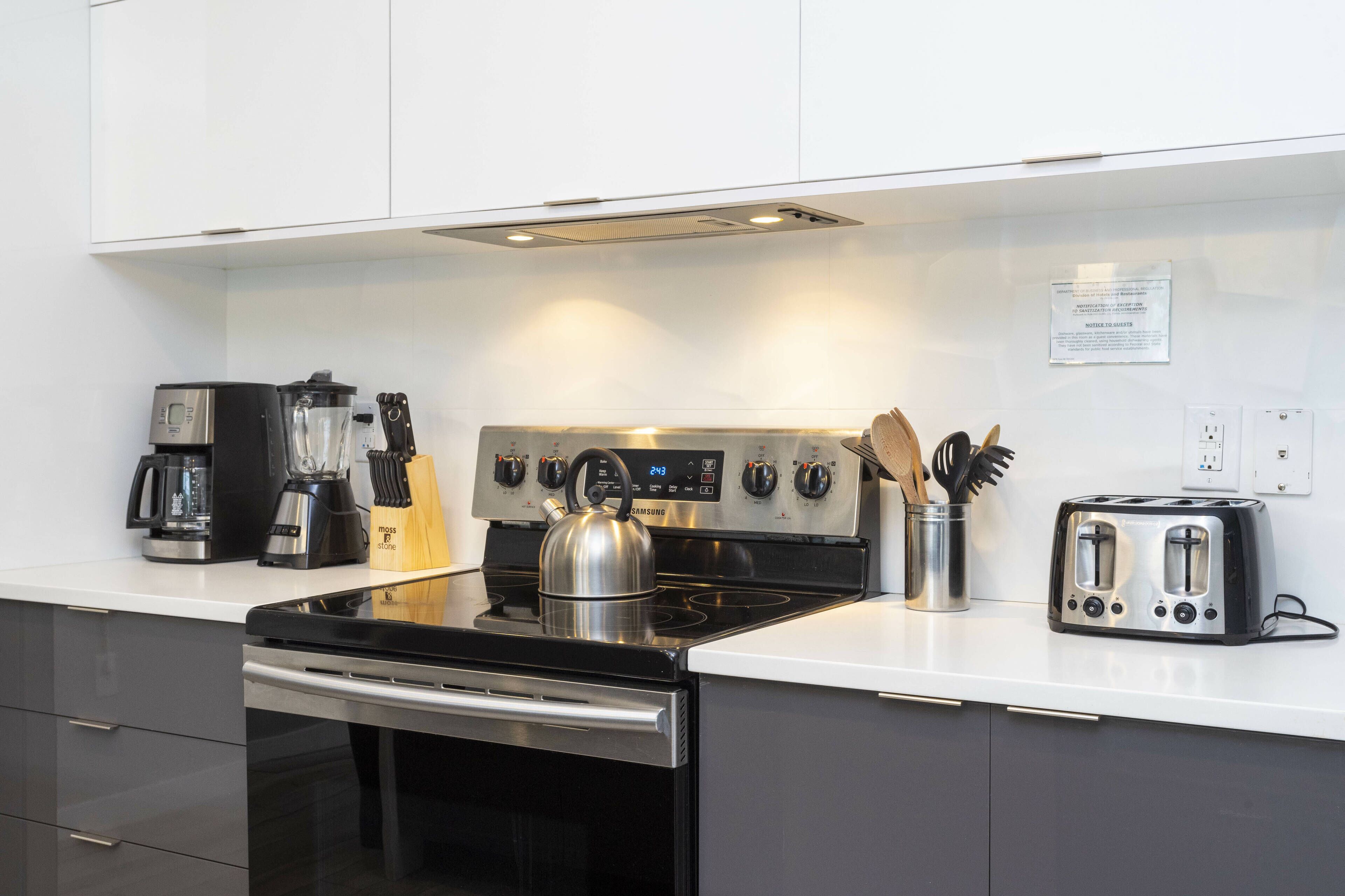 A modern kitchen with a stainless steel stove, a coffee maker, a toaster, and a kettle.