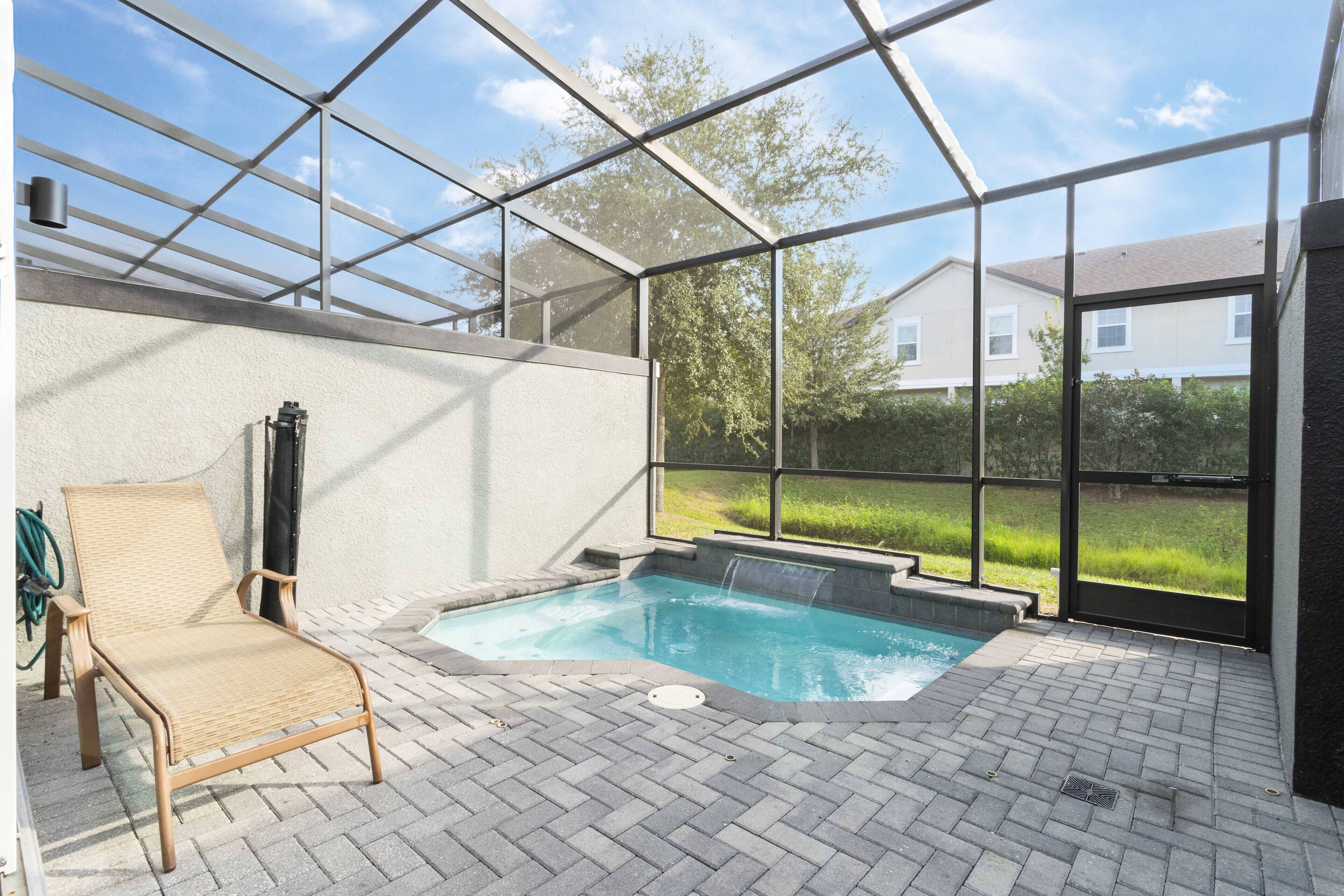A covered outdoor swimming pool with a lounge chair, a hot tub, and a view of a residential area.