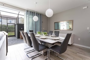 Un espace de salle à manger moderne, doté d’une grande table, de chaises noires et de luminaires suspendus.