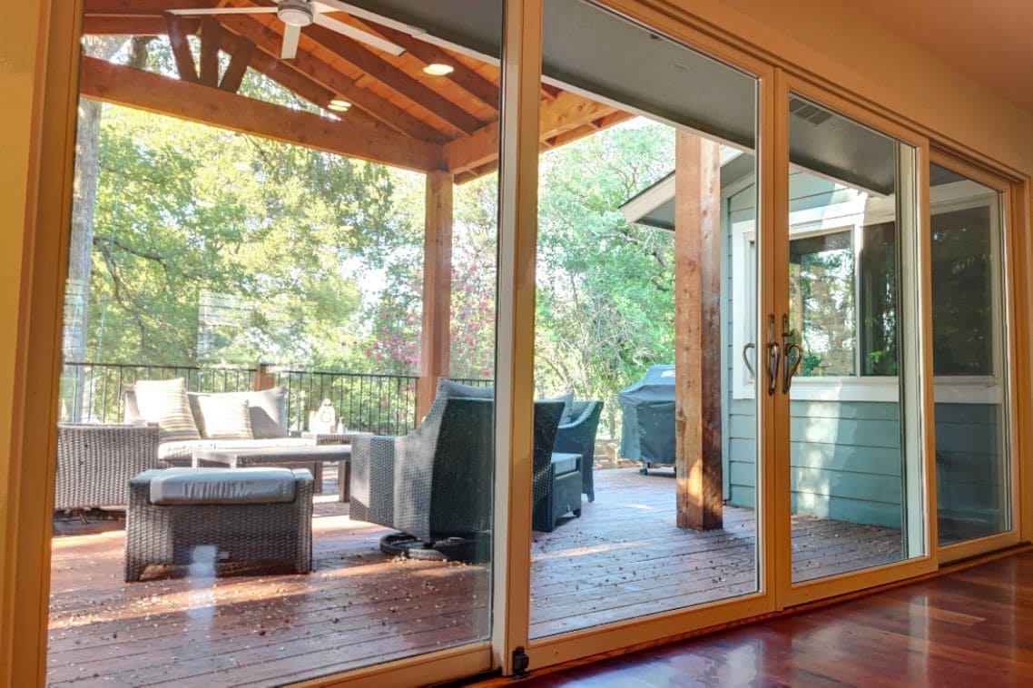 A covered deck with outdoor furniture and a sliding glass door leading to a garden.