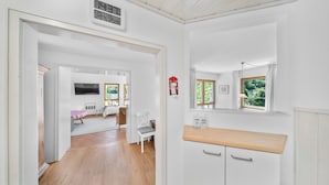 Une pièce avec un plancher en bois, des murs blancs, un coin cuisine doté d’un comptoir en bois, une chaise et un téléviseur.