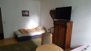 Una habitación pequeña y acogedora con una cama, un televisor sobre un mueble de madera y una mesita.