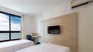A hotel room with two beds, a TV mounted on the wall, a desk, and a window with a view of the sky.