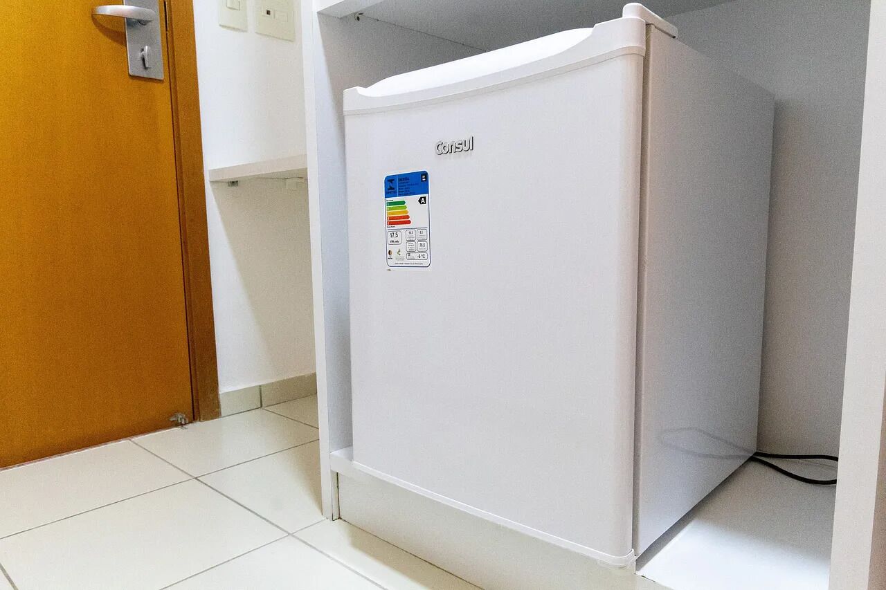 A white refrigerator with a control panel in a corner of a room with white walls and a wooden door.