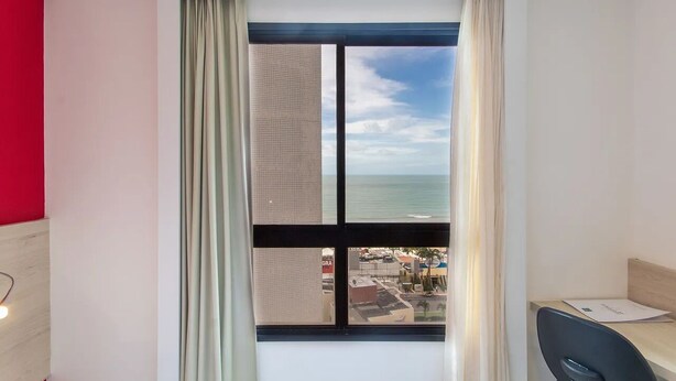 A hotel room with a large window, a desk, and a chair.