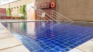 A swimming pool with a tiled floor, a wooden wall with a lifebuoy, and outdoor seating.