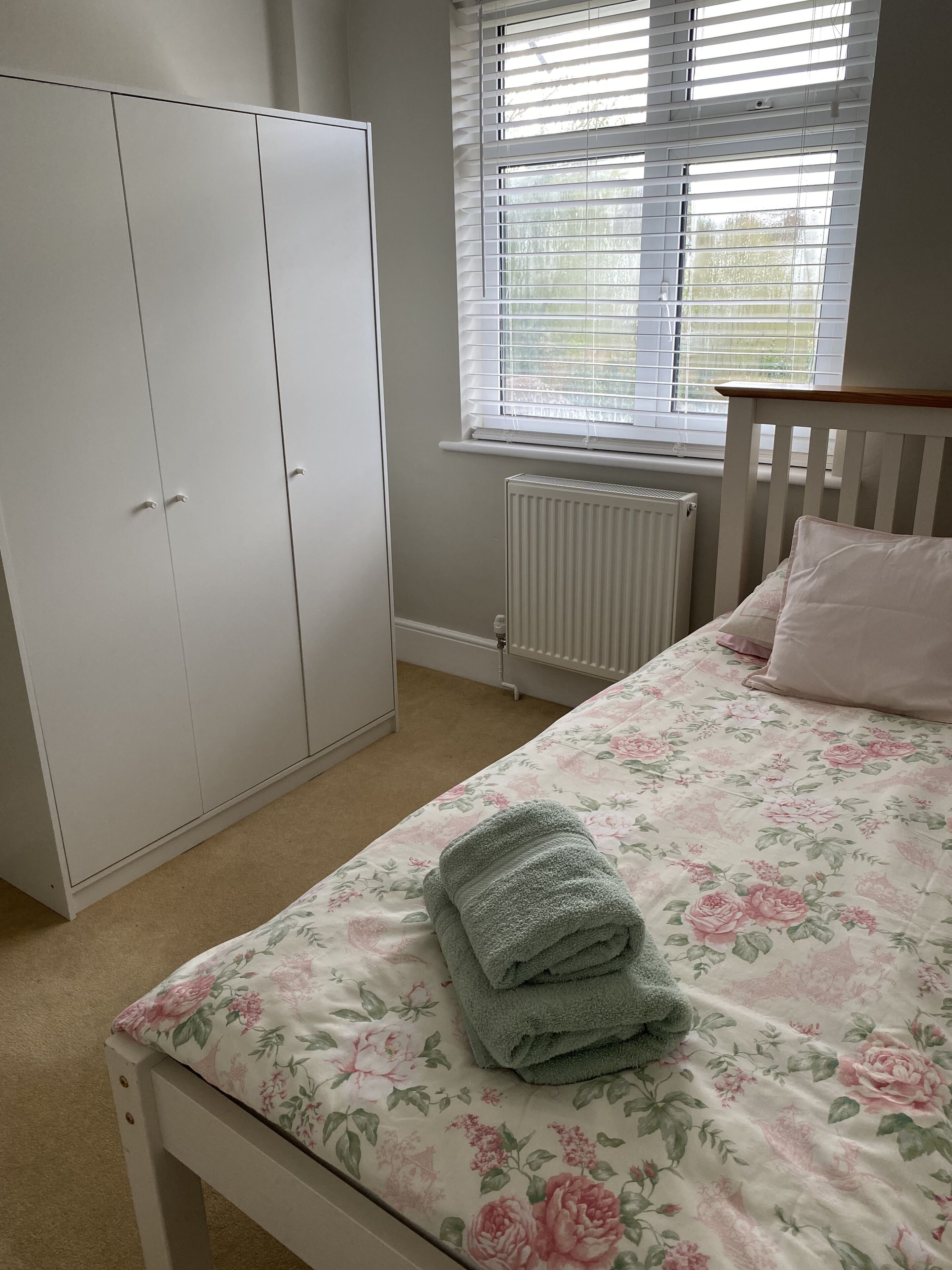 Un dormitorio con cama, armario, radiador y ventana con persianas.