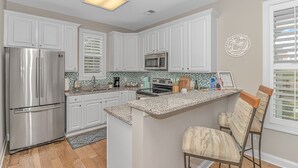 A modern kitchen with white cabinetry, a stainless steel refrigerator, a microwave, and a granite countertop.
