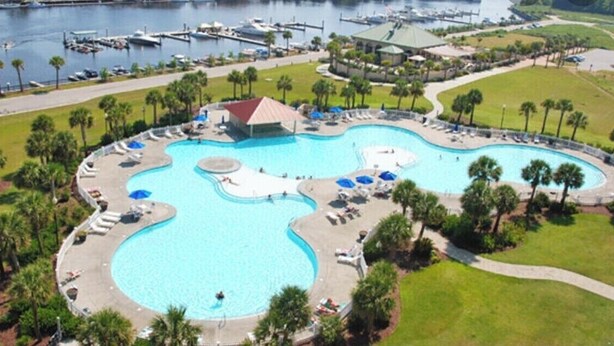 A large, multi-curve swimming pool with lounge areas and a building in the center.