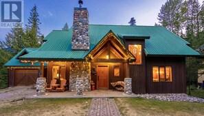 A rustic cabin with a stone chimney, a front porch with chairs, and a brick pathway leading to the entrance.