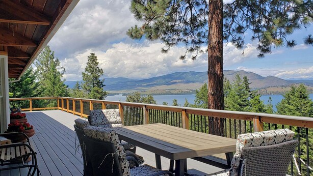 A wooden deck with outdoor furniture, a view of a lake, and surrounding mountains.
