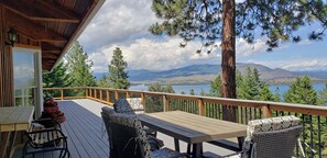 A wooden deck with outdoor furniture, a view of a lake, and surrounding mountains. - Luxury Lodge: Flathead Lake & Wild Horse Island (Big Arm)