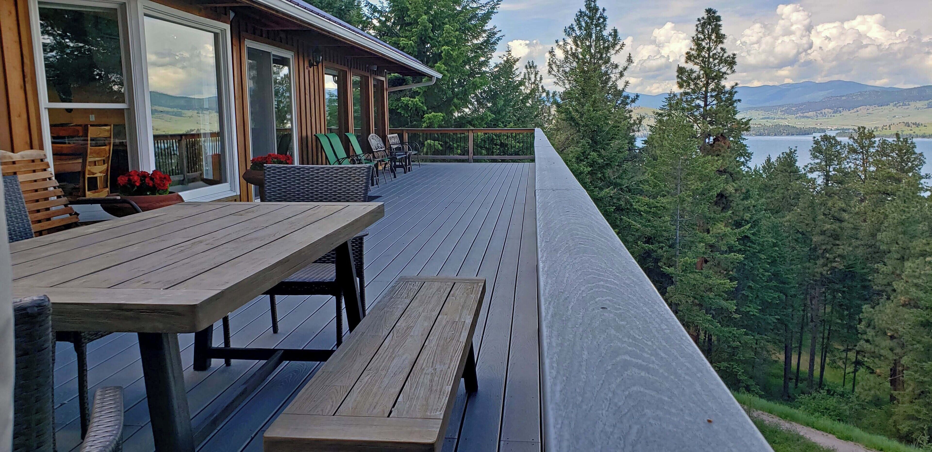 A wooden deck with outdoor furniture, overlooking a lake and forested hills.