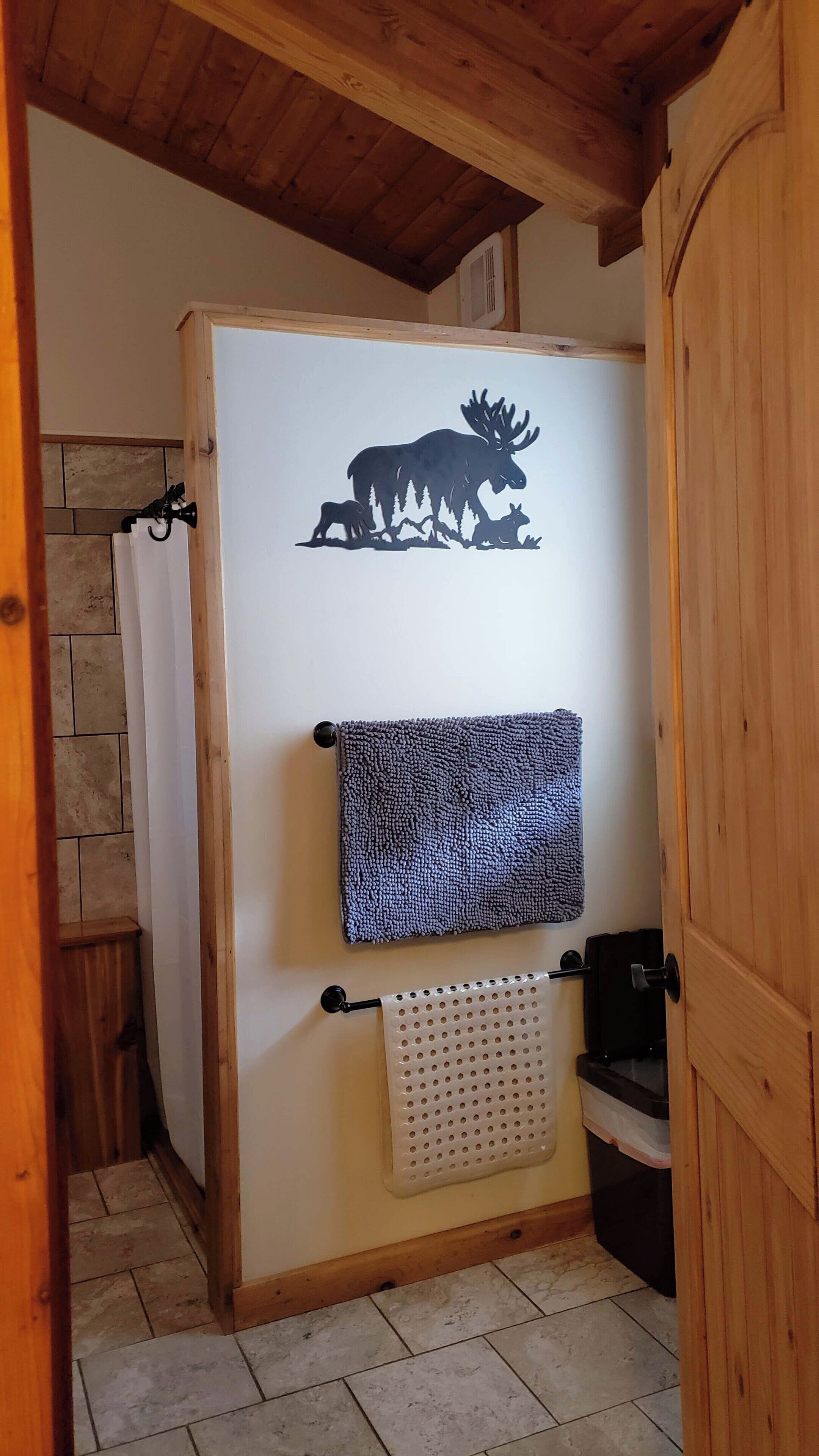 A bathroom with a wooden ceiling, a towel rack with a patterned towel, and a wall decal of a moose.