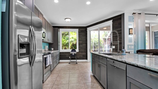 A modern kitchen with stainless steel appliances, grey cabinets, and a large window providing a view of greenery. - Stylish & Bright, Mins to Downtown, Pool, Parking (North Port)