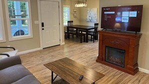 A living room with a fireplace, a TV mounted on a wooden cabinet, a dining area with a table and chairs, and a ceiling fan. - Wilson, Two Bedroom House in Historic Loveland (Loveland)