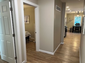 A hallway with a wooden floor, a dining area with a table and chairs, and a bedroom with a bed and a painting on the wall. - Wilson, Two Bedroom House in Historic Loveland (Loveland)