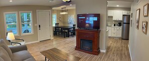 A modern living room with a fireplace, a dining area, and a kitchen with white cabinets. - Wilson, Two Bedroom House in Historic Loveland (Loveland)