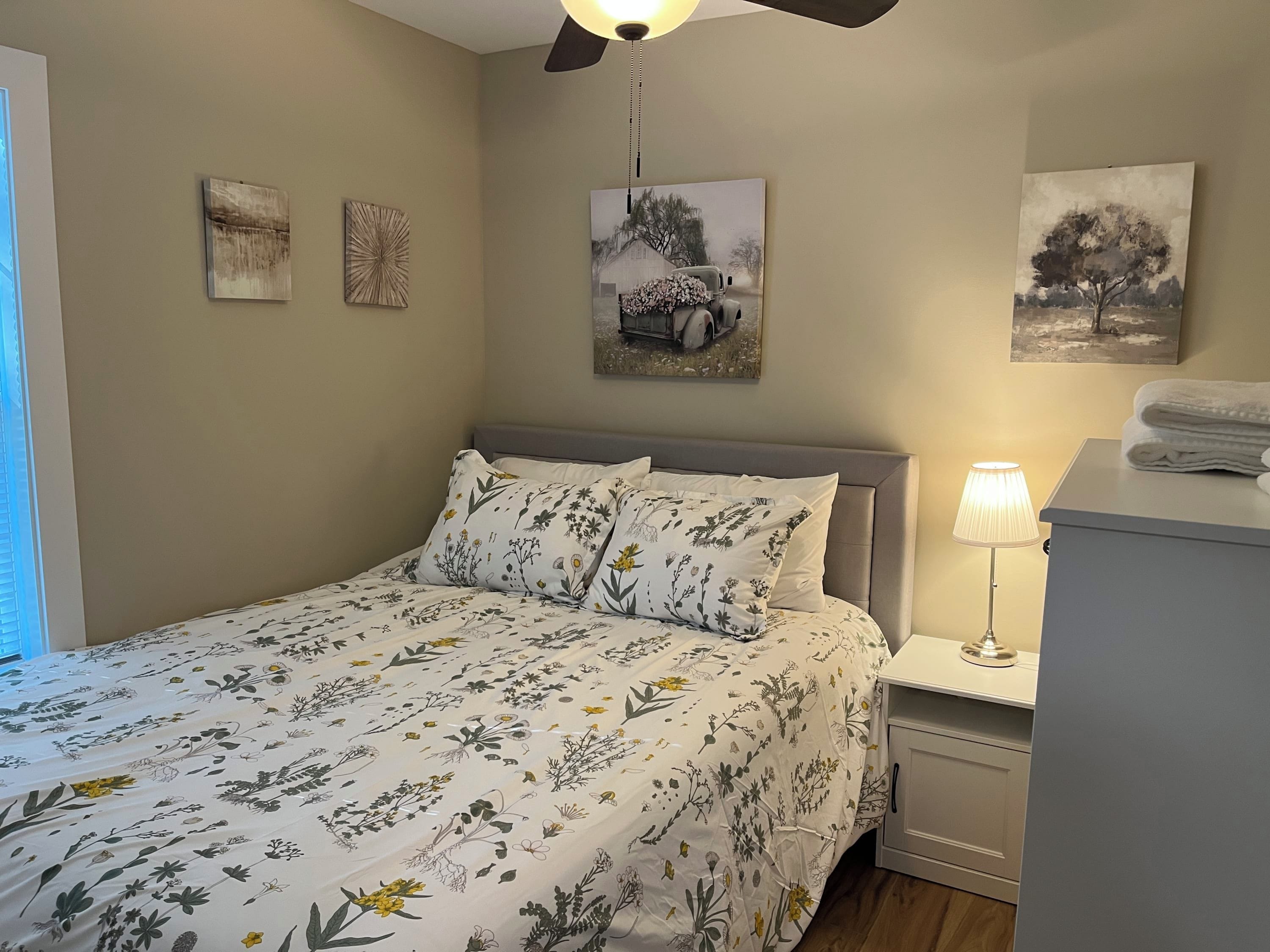 Quarto com cama, mesas de cabeceira, abajur e quadros nas paredes.