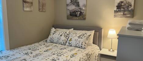 A bedroom with a bed, nightstands, a lamp, and artwork on the walls.