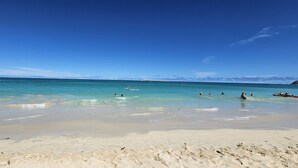 Una playa con aguas turquesas cristalinas, orilla arenosa y montañas distantes.