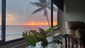 Una habitación con vistas al océano al atardecer, una planta en maceta y una silla.