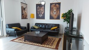 Een woonkamer met een zwarte leren bank, een bijzettafeltje, een kamerbreed tapijt en drie ingelijste dierenportretten aan de muur.