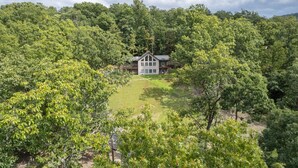 Ein großes Haus, umgeben von dichtem Wald, mit einem gepflegten Rasen davor.