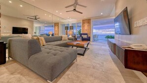 A modern living room with a sectional sofa, a coffee table, a TV, and a view of the ocean.