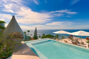 Una piscina con vista sull'oceano, lettini e ombrelloni.