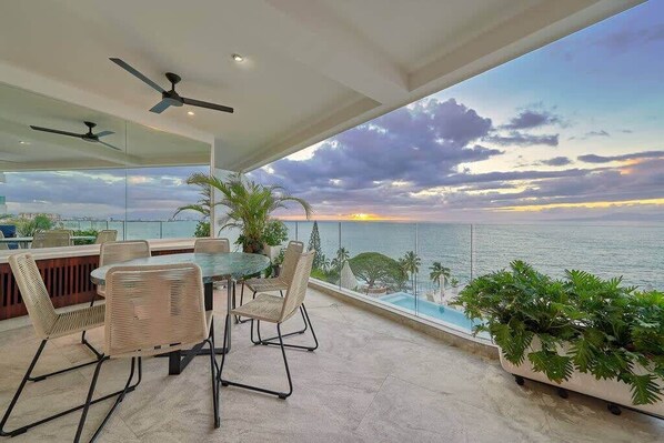 Un balcone con tavolo e sedie, vista su un corpo d'acqua e un tramonto.