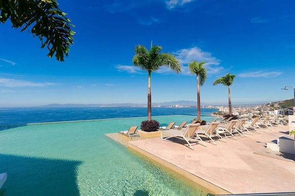 An infinity pool with clear blue water, palm trees, and lounge chairs.