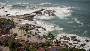 A coastal area with rocky terrain, a beach, and a row of buildings with red-tiled roofs.