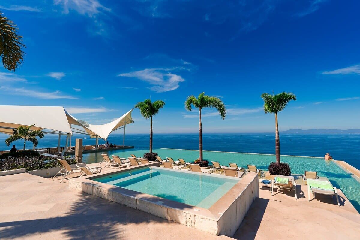 Un espace aménagé au bord de la piscine, avec des chaises longues et des palmiers, offrant une vue sur l’océan.
