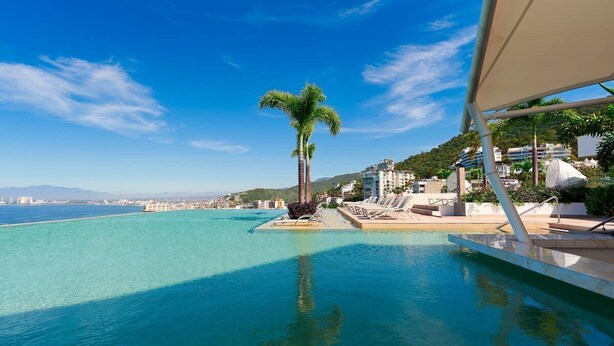 A pool area with clear blue water, a palm tree, and lounge chairs.