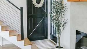 Un intérieur moderne avec un escalier, une porte noire ornée d’une guirlande, une plante en pot et une cheminée.