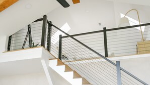 Un intérieur moderne avec un escalier menant à un niveau supérieur, un ventilateur de plafond et un lit doté d’une tête de lit.