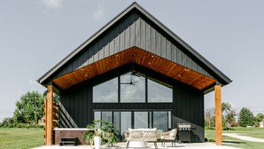 Un bâtiment moderne doté d’une grande baie vitrée, de poutres en bois et d’un espace extérieur aménagé avec des sièges.