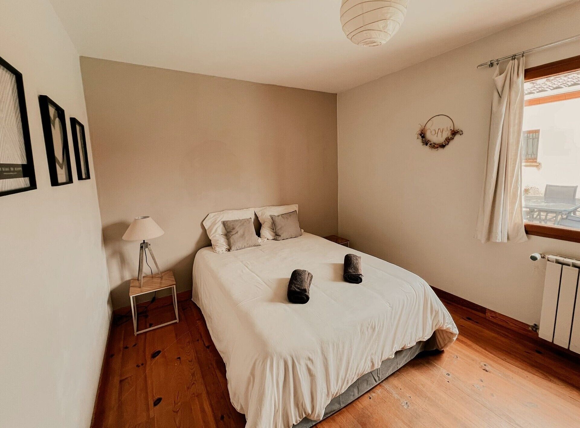 Un dormitorio con cama, mesita de noche, lámpara y ventana con cortinas.
