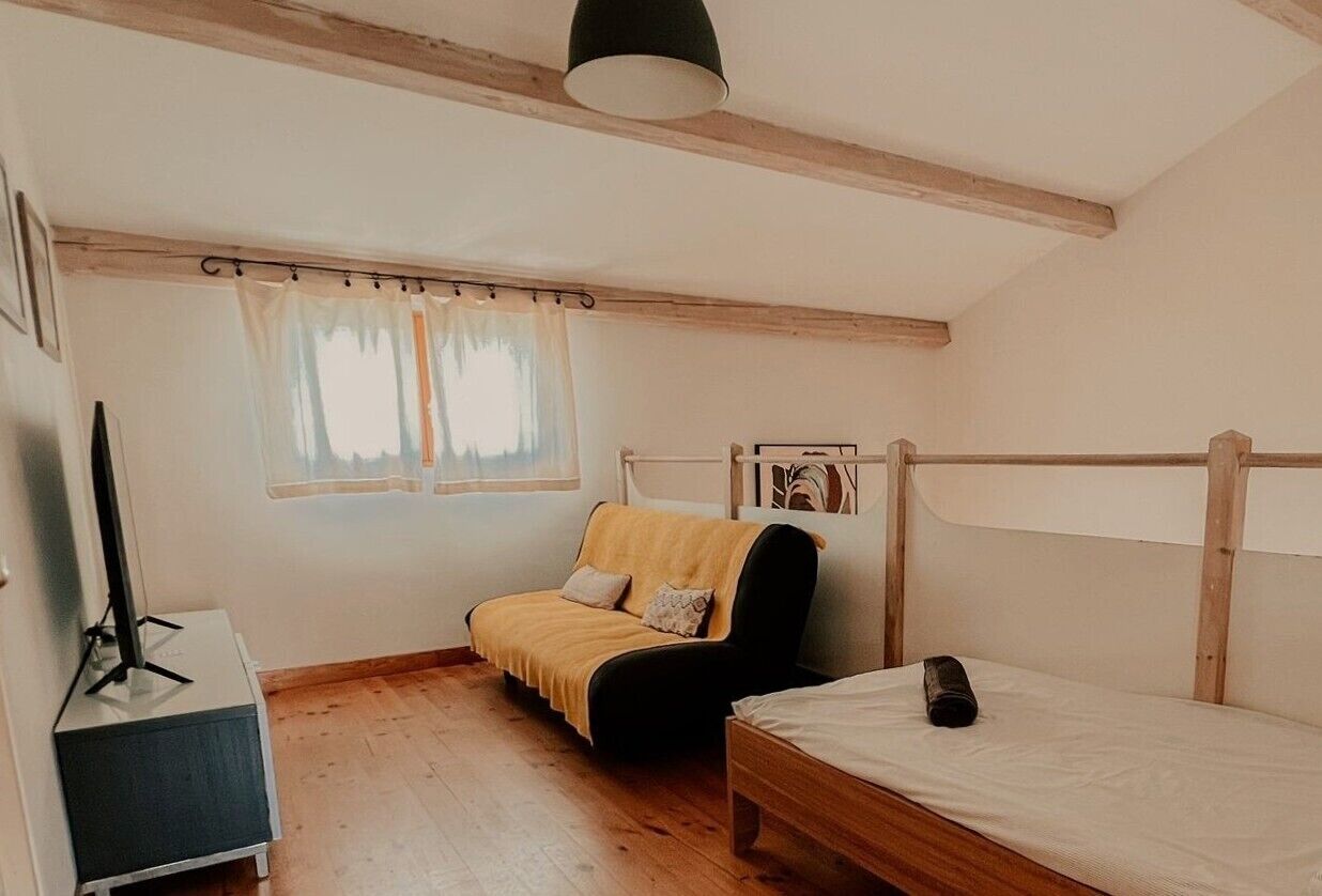 Ein kleiner, gemütlicher Raum mit Holzboden, einem Bett, einer Couch und einem Fernsehschrank.