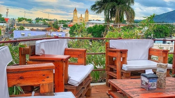A wooden deck with outdoor seating, a view of a historic building with two towers, and a palm tree in the background.