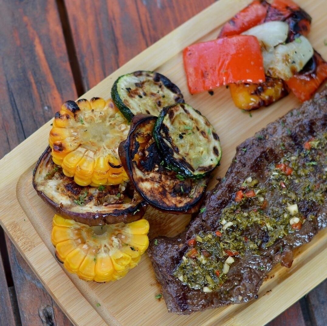 Een houten snijplank met gegrilde groenten en een steak, wat een maaltijdsetting doet vermoeden.